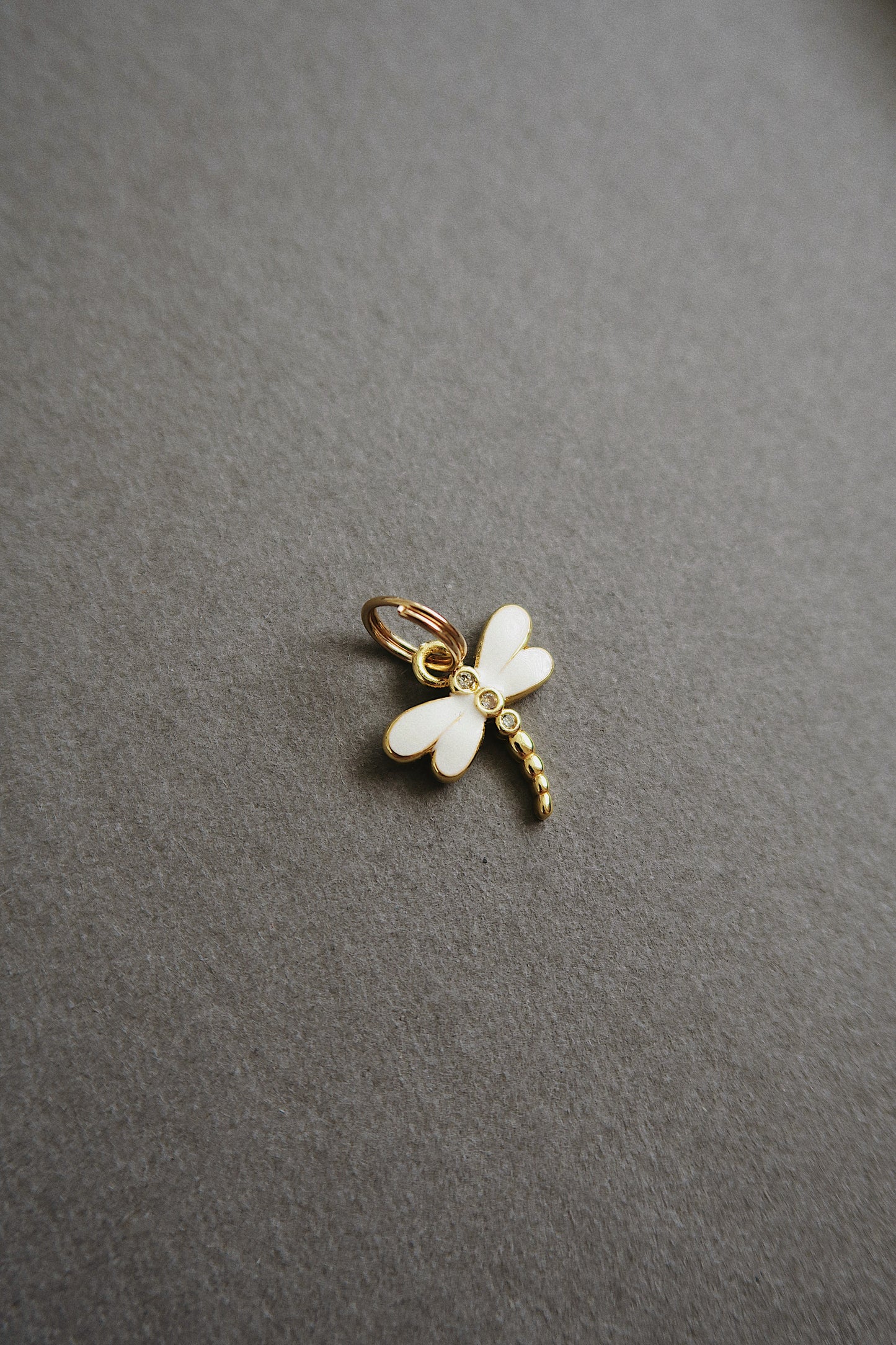 Gold and white dragonfly charm on a gray background