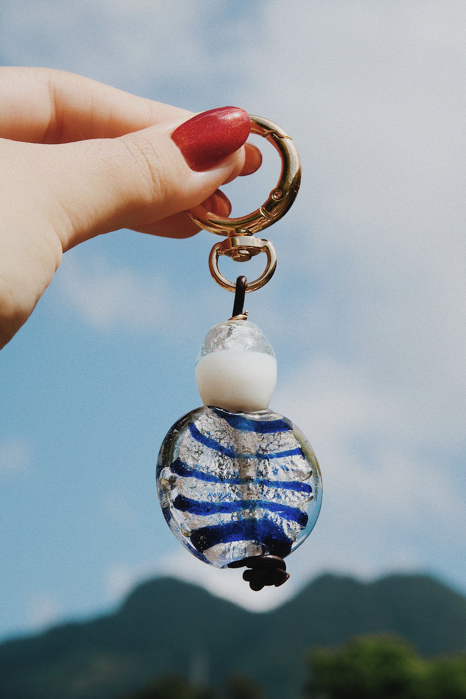 Keychain with blue and silver striped bead held by a hand against a blurred natural background. Tres picachos.